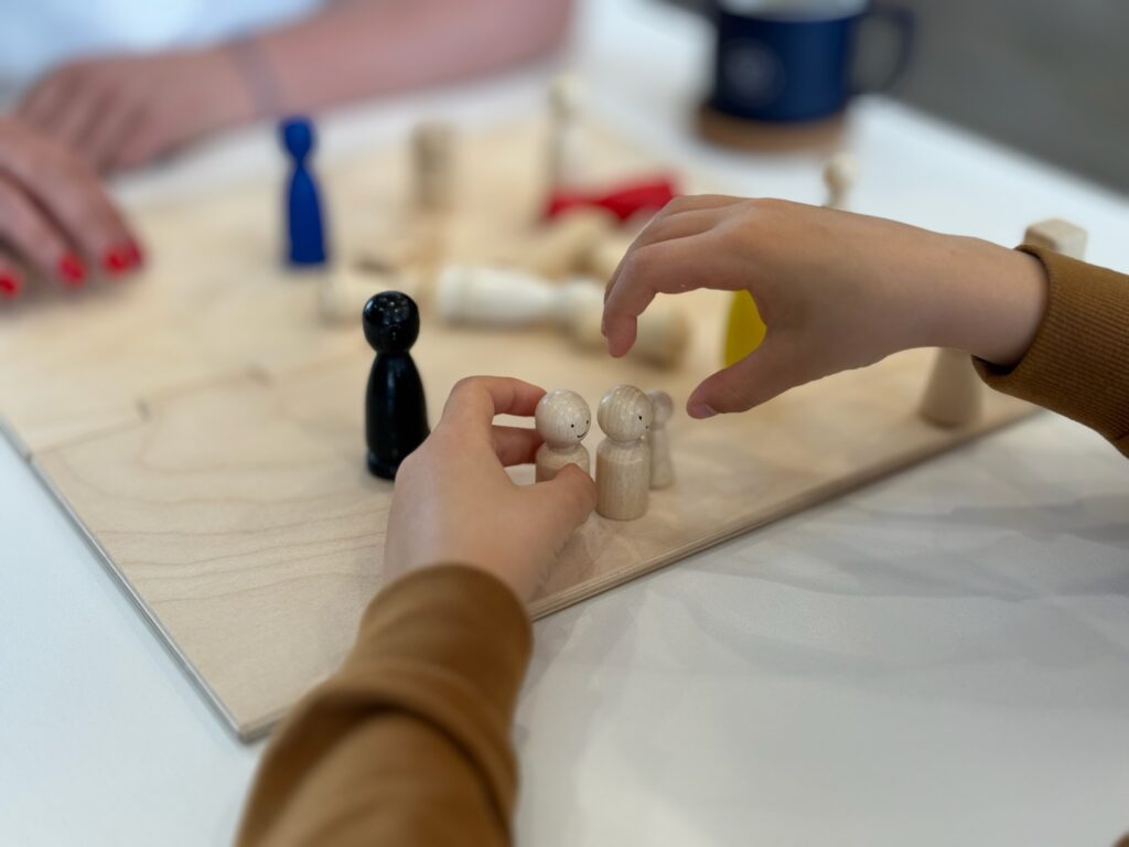 Kinderhände stellen kleine Holzfiguren auf einem Familienbrett auf – Symbol für die Aufstellung einer Familie und ihres Netzwerks