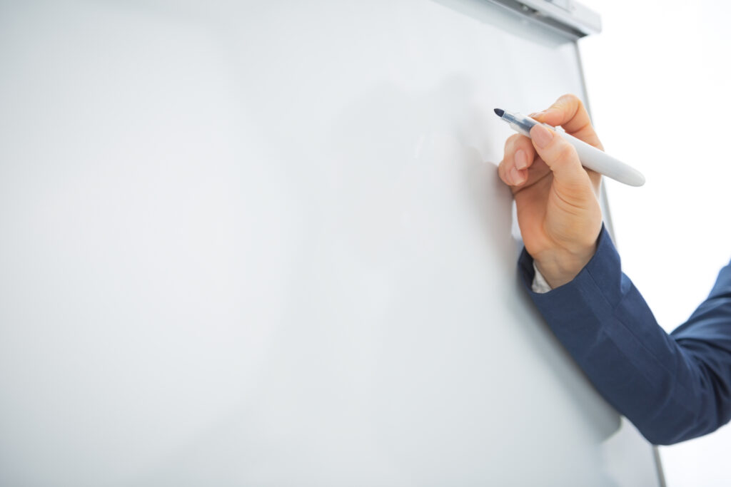 Hand schreibt mit einem Marker auf ein leeres Flipchart – Symbolbild für fachliche Analyse und Wirkmechanismen
